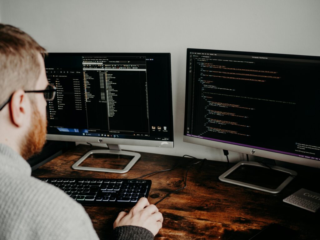 Software developer working on code with dual monitors in a home office setting.