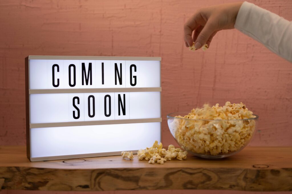 A hand reaching for popcorn next to an illuminated 'Coming Soon' sign, creating a cinematic feel.